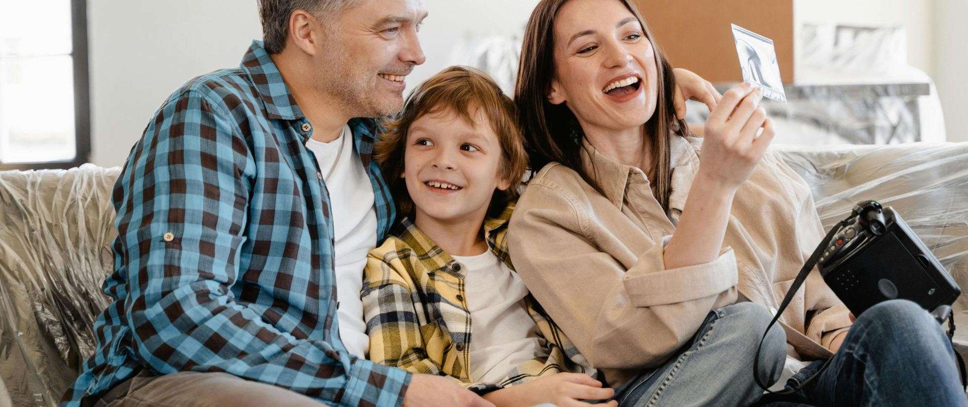 A cheerful family enjoys time together on a couch surrounded by moving boxes in their new home.